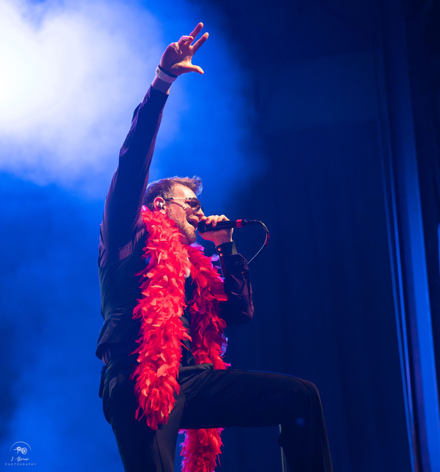The singer raising one hand in blue light, red boa